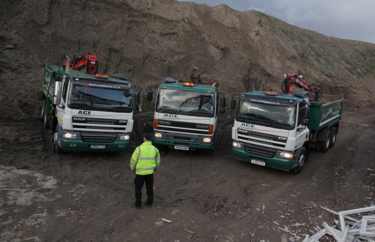 Man in high vis standing in front of 3 Ace vehicles.